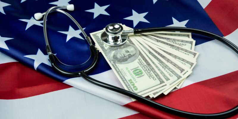 A stethoscope with American currency on top of an American flag